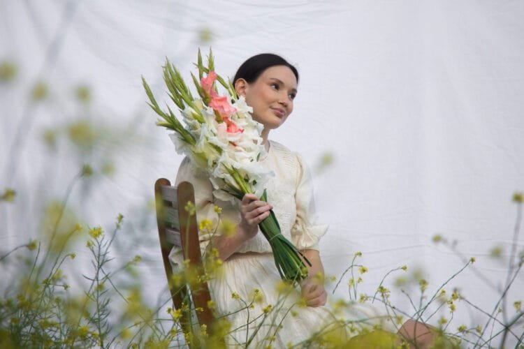 a woman surrounded by a mysterious aura, holding a delicate yet captivating flower in her hand.